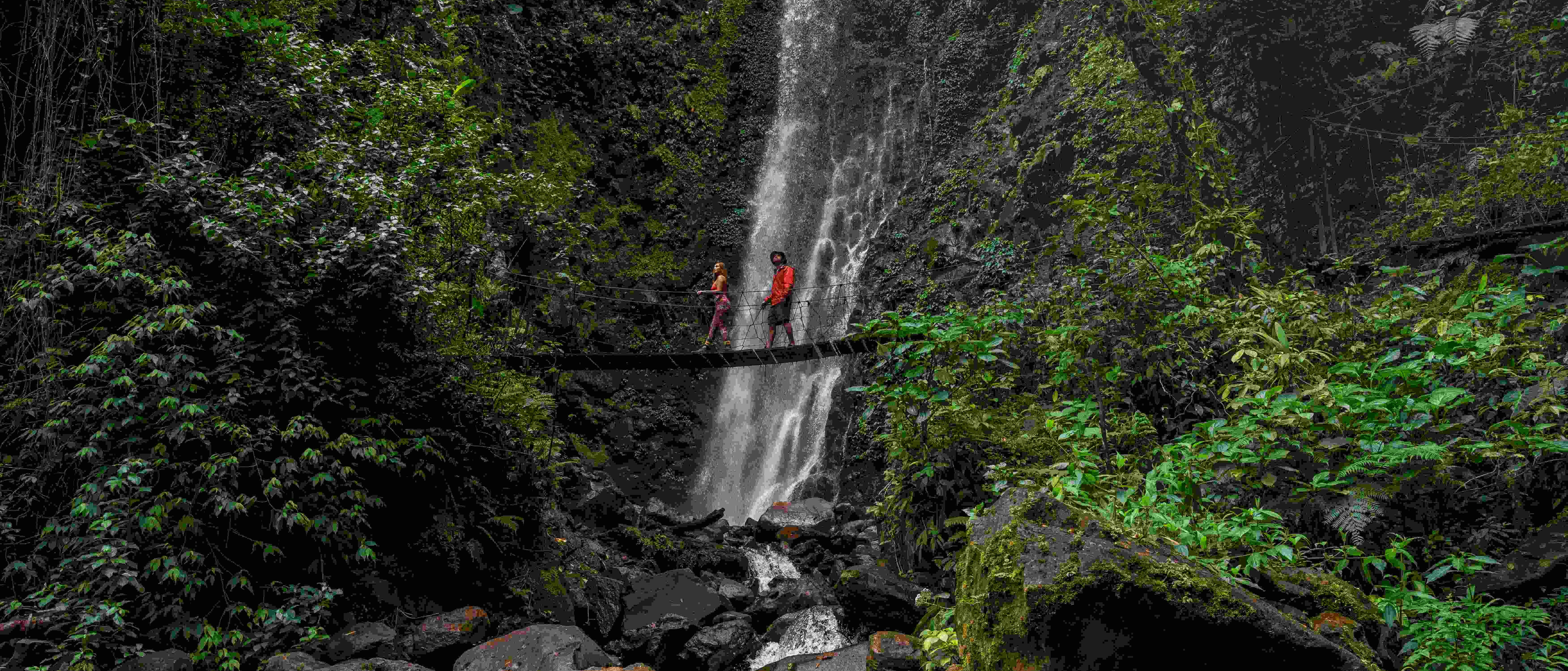 Two people crossing a hanging bridge in front of a stunning waterfall in Monteverde, Costa Rica.