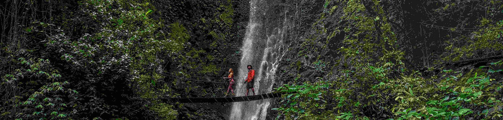 Dos personas cruzando un puente colgante frente a una impresionante cascada en Monteverde, Costa Rica.