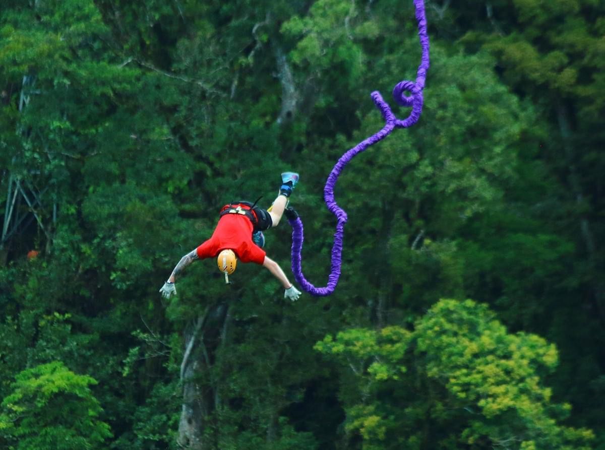 A bungee jumper mid-dive with a vibrant green forest backdrop at Monteverde Extremo Park.