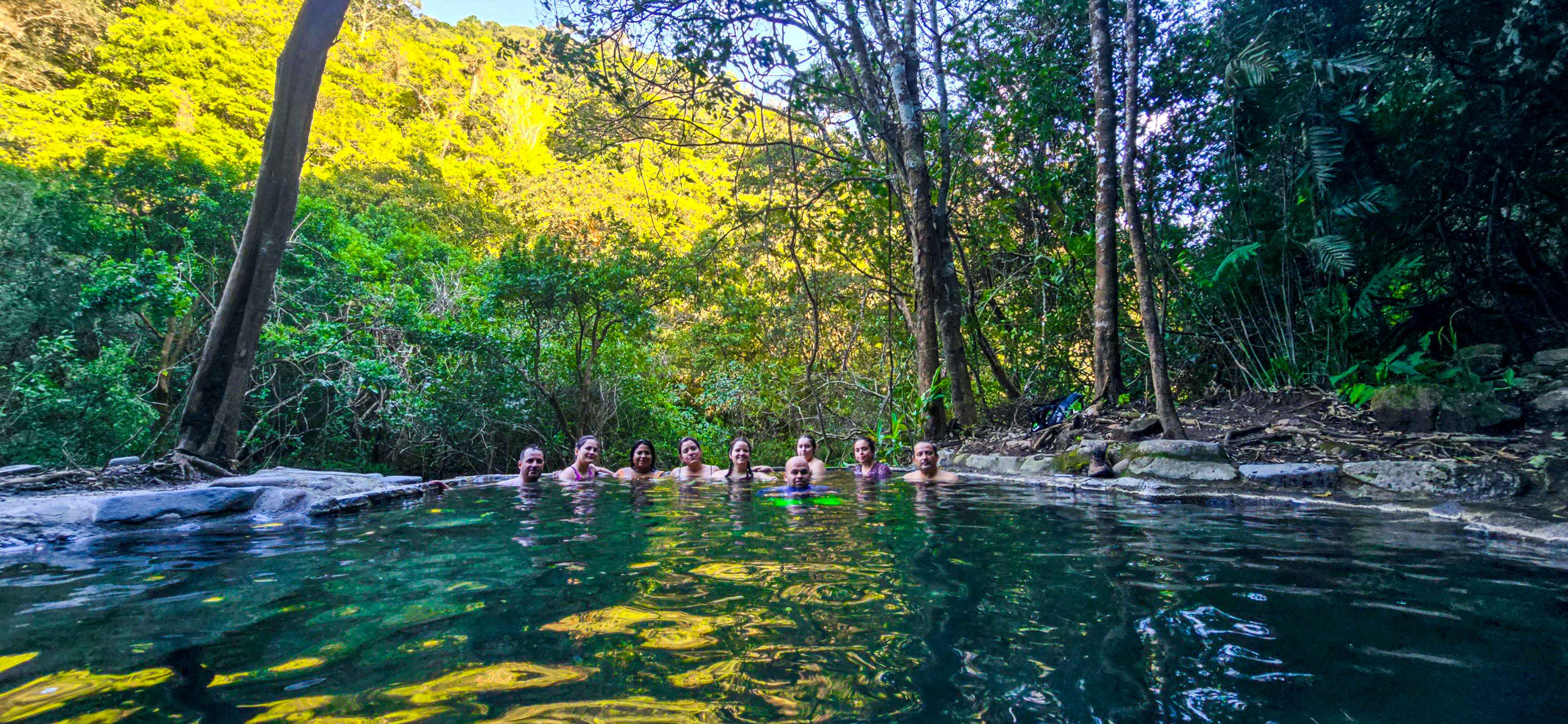 A group of people enjoying a natural hot spring surrounded by lush green forest in Monteverde, Costa Rica.